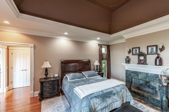 The primary bedroom is located on the main floor. The bedroom features a cozy fireplace, a tray ceiling, and beautiful hardwood floors. | Image 19