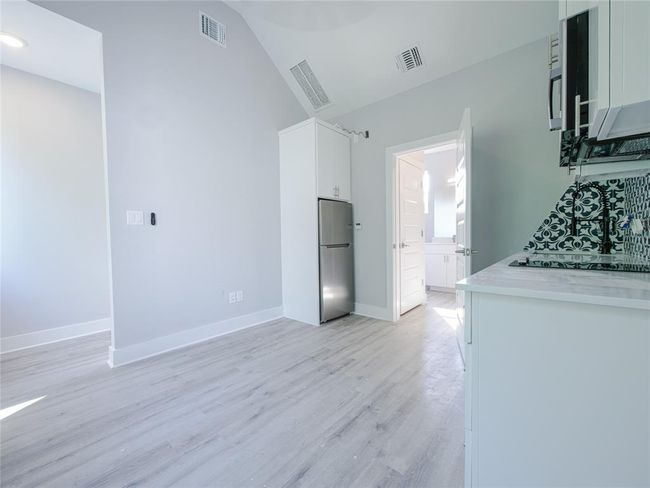 Kitchen with stainless steel refrigerator, white cabinetry, light wood-style floors, black stovetop, and light countertops | Image 28
