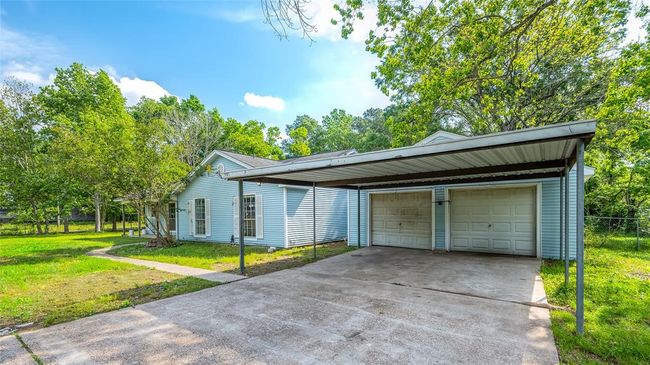 Spacious two-car garage with additional covered parking, surrounded by lush greenery. | Image 5