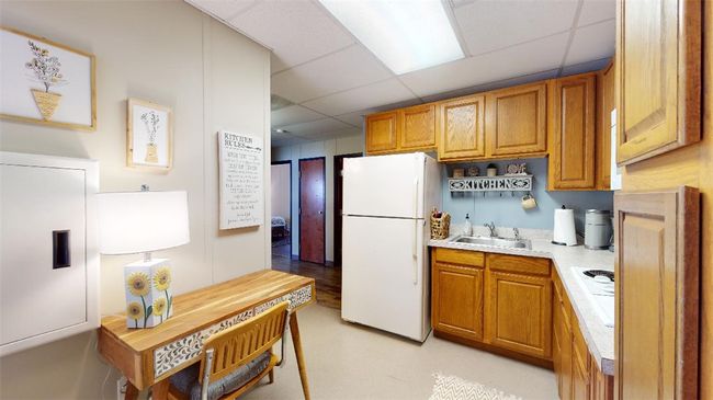 Kitchen with freestanding refrigerator, a paneled ceiling, a sink, light countertops, and brown cabinets | Image 6