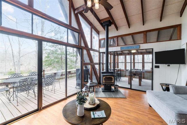 Living room with a wall of windows, wood finished floors, a ceiling fan, beam ceiling, and a wood stove | Image 6