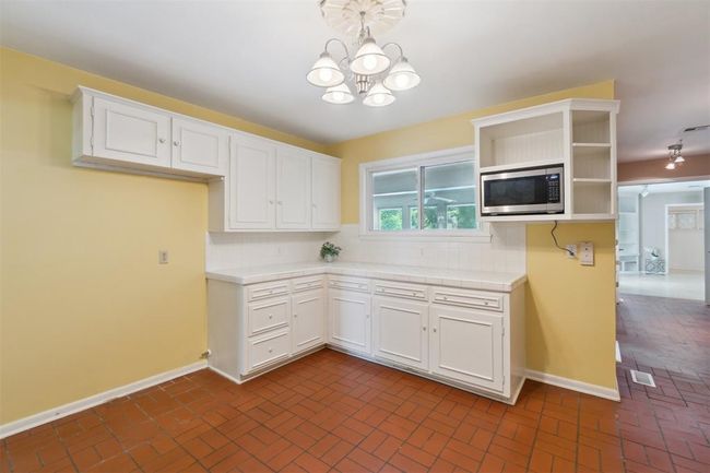 Kitchen with stainless steel microwave, brick patterned floors, a chandelier, open shelves, and tile counters | Image 13