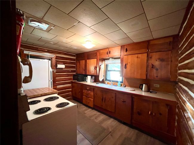 Kitchen with rustic walls, brown cabinetry, light countertops, black microwave, and freestanding refrigerator | Image 16