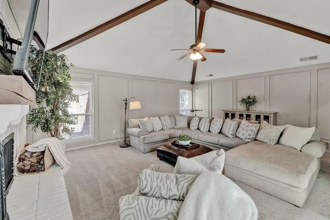 Living room with a brick fireplace, a decorative wall, carpet, beam ceiling, and a ceiling fan | Image 8
