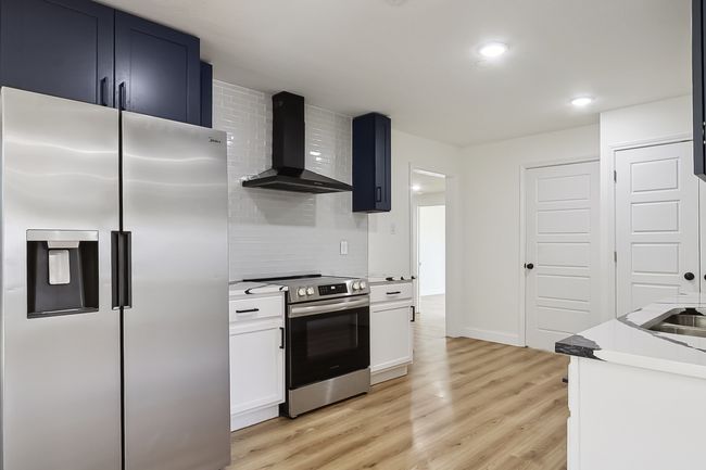 Kitchen featuring white cabinets, decorative backsplash, appliances with stainless steel finishes, light countertops, and wall chimney range hood | Image 7