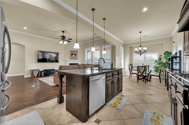 Kitchen featuring arched walkways, ceiling fan, a breakfast bar area, crown molding, and a fireplace | Image 6