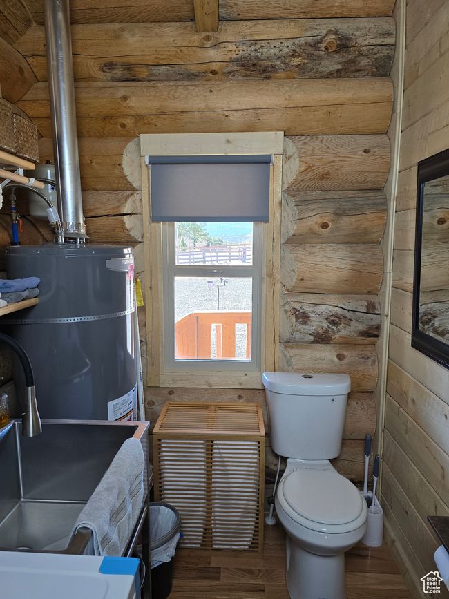 Bathroom featuring toilet, strapped water heater, wood finished floors, and log walls | Image 116