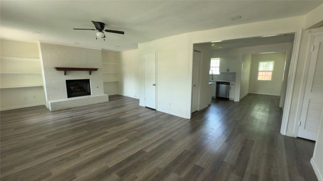 Unfurnished living room featuring a ceiling fan, dark wood-style flooring, built in shelves, and a brick fireplace | Image 17