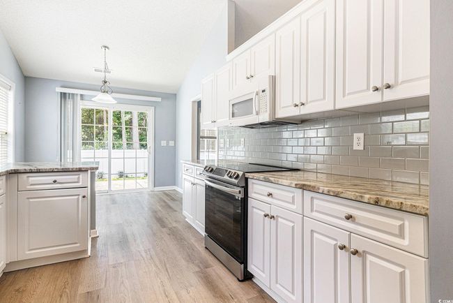 Kitchen featuring stainless steel electric range oven, light wood-type flooring, backsplash, lofted ceiling, and white cabinets | Image 17