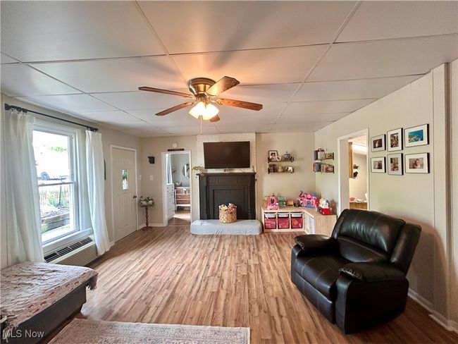 Living room with wood finished floors, baseboards, a drop ceiling, ceiling fan, and a fireplace | Image 7