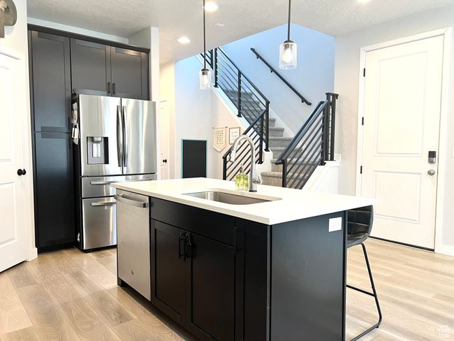 Kitchen featuring appliances with stainless steel finishes, light wood-style flooring, light countertops, a center island with sink, pendant lighting and front door. | Image 4