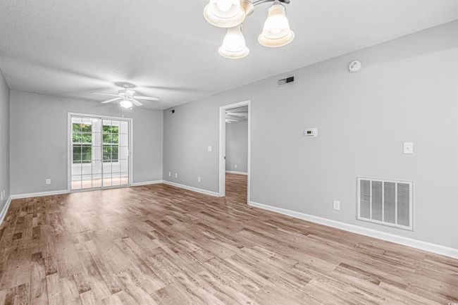 Spare room featuring light wood-type flooring, a ceiling fan, a chandelier, a smoke detector, and a textured ceiling | Image 12