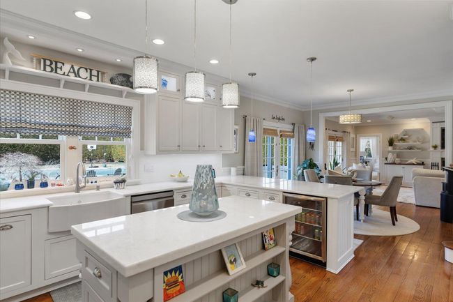 Kitchen featuring light countertops, a center island, a sink, beverage cooler, and stainless steel dishwasher | Image 9