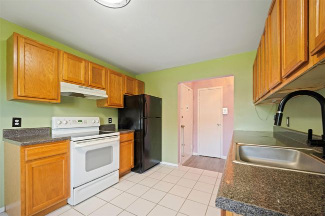 Kitchen with freestanding refrigerator, white electric range oven, under cabinet range hood, a sink, and light tile patterned floors | Image 5