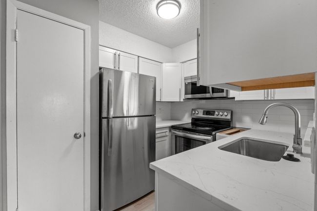 Kitchen featuring a textured ceiling, a sink, stainless steel appliances, backsplash, and light stone countertops | Image 10