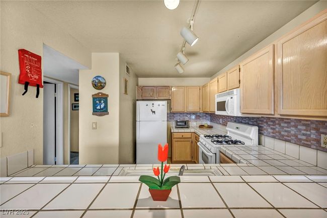 Kitchen with tile counters, light brown cabinets, decorative backsplash, and white appliances | Image 32