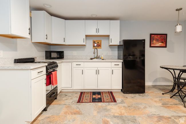 Kitchen with a sink, stone finish flooring, black appliances, light countertops, and white cabinets | Image 23