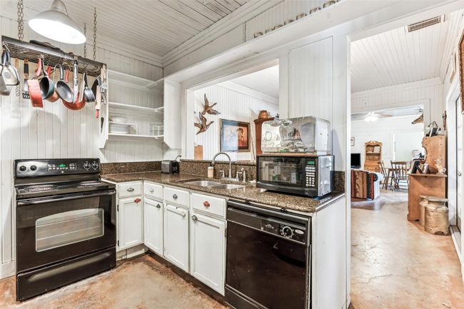 Kitchen featuring black appliances, concrete floors, open shelves, dark stone counters, and crown molding | Image 16
