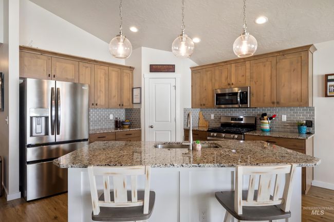 Kitchen featuring stainless steel appliances, decorative backsplash, lofted ceiling, brown cabinets, and decorative light fixtures | Image 4