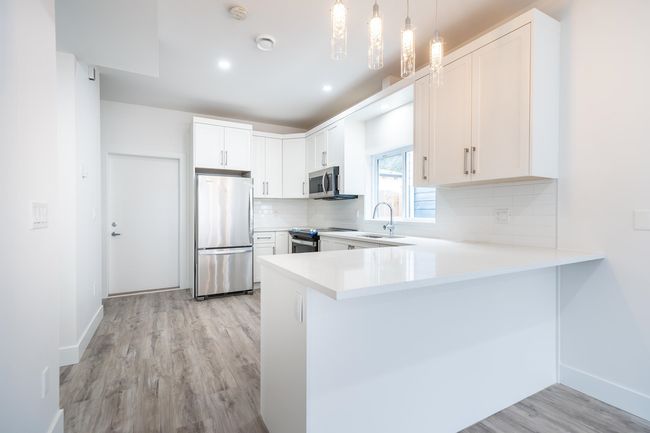 Kitchen with appliances with stainless steel finishes, a peninsula, light wood finished floors, decorative backsplash, and a sink | Image 8