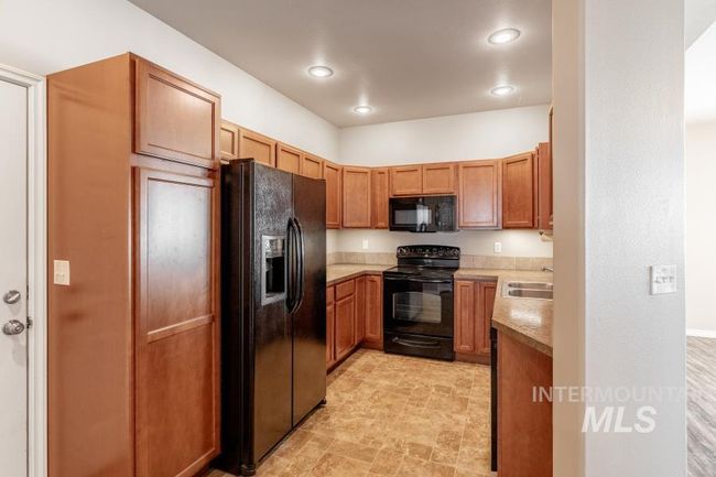 Kitchen with black appliances, light countertops, stone finish floors, recessed lighting, and brown cabinetry | Image 6