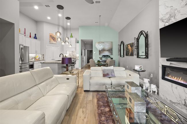 Living area with light wood-style flooring, a glass covered fireplace, and high vaulted ceiling | Image 4
