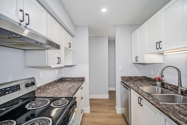 Kitchen featuring appliances with stainless steel finishes, under cabinet range hood, a sink, baseboards, and light wood-type flooring | Image 5