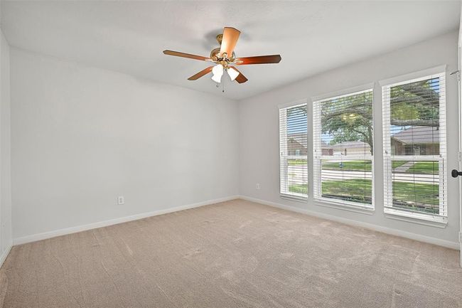 The third bedroom offers plush carpeting, a lighted ceiling fan, a spacious walk-in closet, and a charming front-facing window that fills the space with natural light. | Image 21