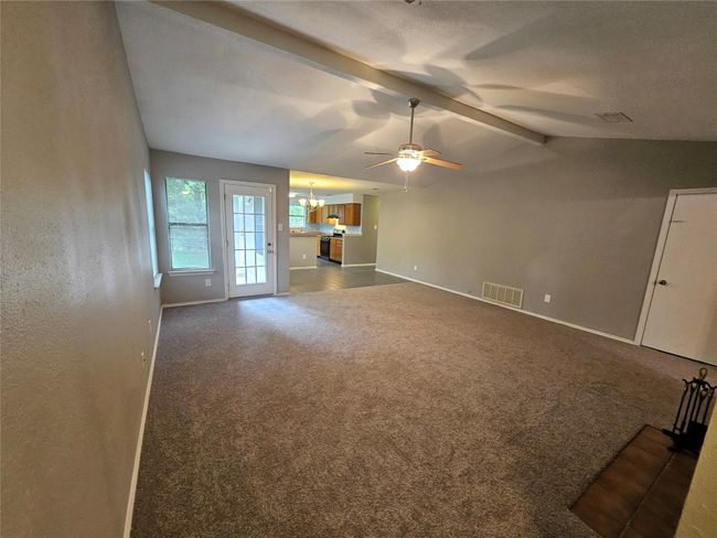 Unfurnished living room with baseboards, visible vents, ceiling fan with notable chandelier, dark carpet, and lofted ceiling with beams | Image 10