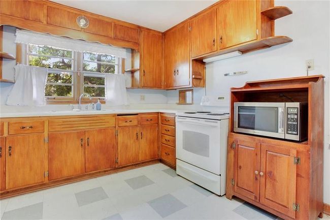 Kitchen with stainless steel microwave, white electric range oven, open shelves, light flooring, and brown cabinetry | Image 8