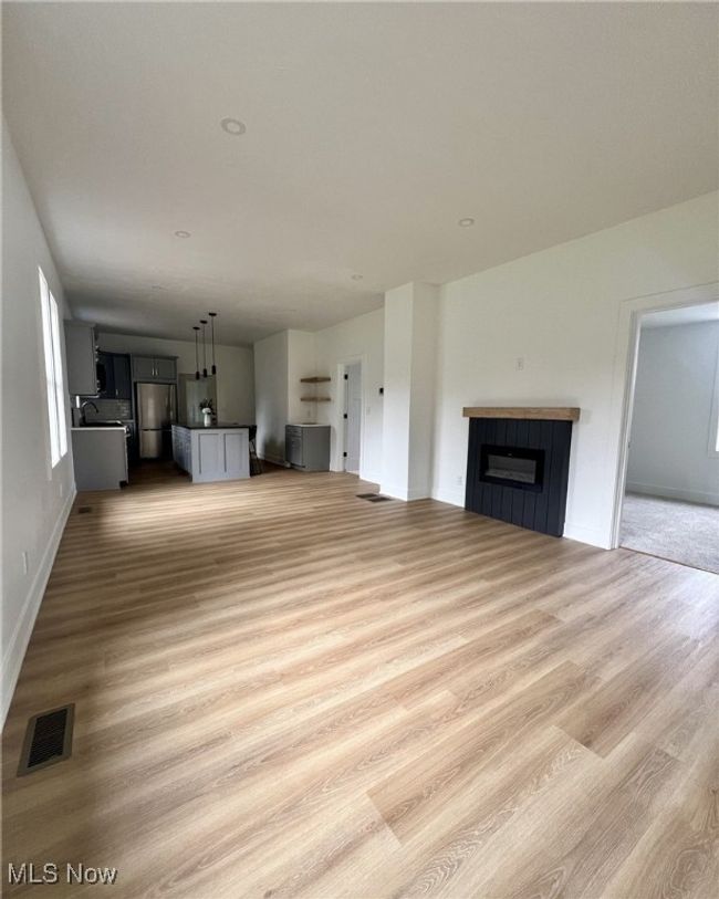 Unfurnished living room featuring a tiled fireplace, visible vents, baseboards, and light wood finished floors | Image 6