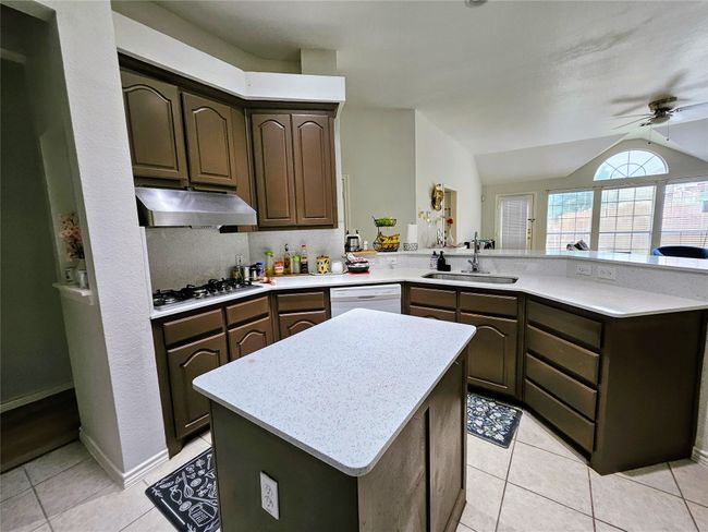 Kitchen with under cabinet range hood, stainless steel gas stovetop, white dishwasher, a peninsula, and ceiling fan | Image 11