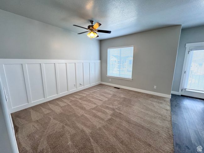 Unfurnished room featuring ceiling fan, visible vents, a decorative wall, a textured ceiling, and wainscoting | Image 5