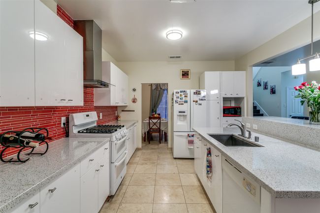 Kitchen with white appliances, a sink, wall chimney exhaust hood, tasteful backsplash, and white cabinets | Image 11