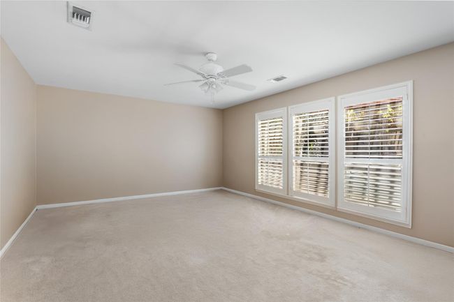 This spacious primary bedroom offers a blank canvas ready for your personal touch. With neutral tones, plush carpeting, and large windows adorned with plantation shutters, the room is filled with natural light and offers a serene retreat. The open layout provides endless possibilities to design your ideal space. | Image 24