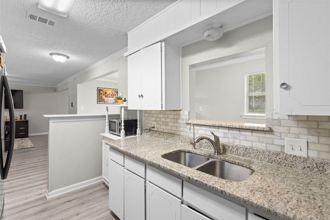 Kitchen with a sink, light wood-style flooring, white cabinetry, tasteful backsplash, and visible vents | Image 14