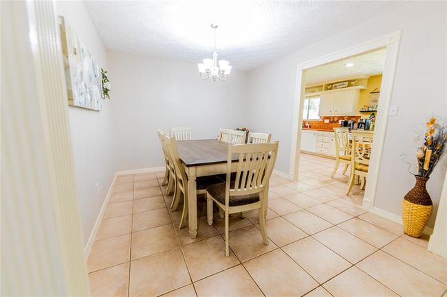 This dining area features a spacious setting with tiled flooring, and a bright chandelier. It opens into a cozy kitchen, creating a welcoming space for meals and gatherings. | Image 13