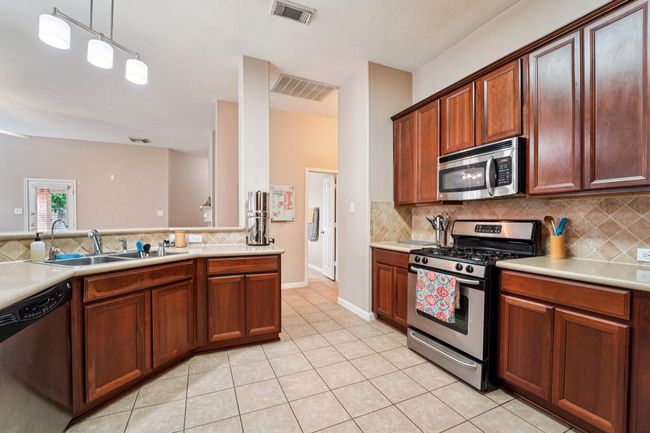 This kitchen features rich wood cabinetry, stainless steel appliances, and a gas stove. It has a spacious layout with a double sink, ample counter space, and a tiled backsplash, creating a warm and functional cooking area. | Image 4