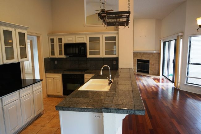 Kitchen with black appliances, tile countertops, a sink, a high ceiling, and ceiling fan | Image 10