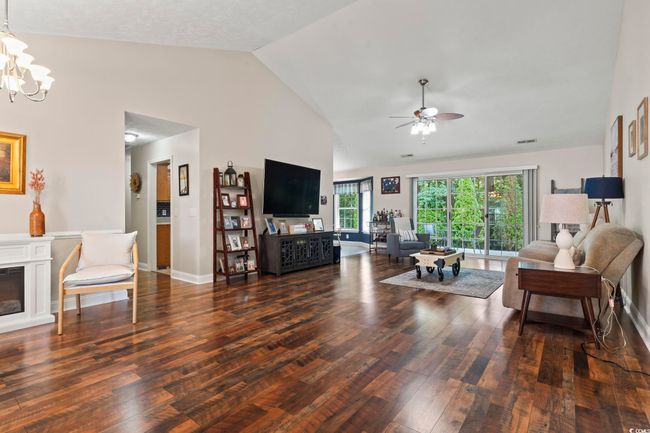 Living room featuring wood finished floors, a ceiling fan, a chandelier, a glass covered fireplace, and high vaulted ceiling | Image 8