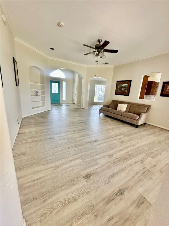 Living area with arched walkways, crown molding, a ceiling fan, and wood finished floors | Image 6