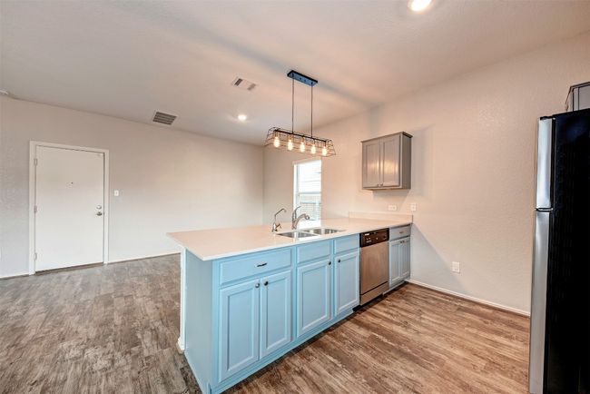 Kitchen featuring appliances with stainless steel finishes, a sink, a peninsula, wood finished floors, and light countertops | Image 12