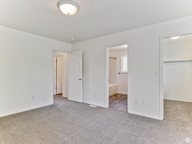 Unfurnished bedroom with ensuite bath, a spacious closet, carpet flooring, and baseboards | Image 8