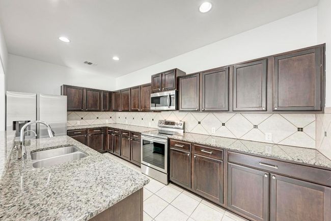 Kitchen with appliances with stainless steel finishes, a sink, dark brown cabinets, backsplash, and light stone counters | Image 19