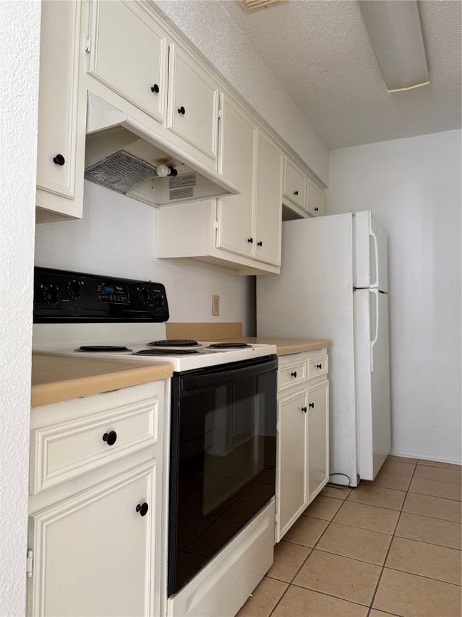 Kitchen featuring ventilation hood, light countertops, light tile patterned flooring, stove, and fridge | Image 5