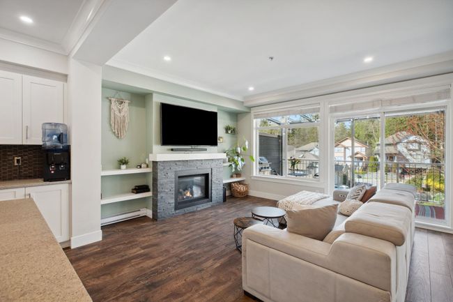 Living room with baseboard heating, baseboards, a fireplace, crown molding, and dark wood-type flooring | Image 7