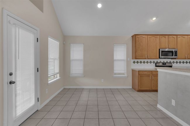 Kitchen featuring stainless steel microwave, vaulted ceiling, light countertops, decorative backsplash, and range | Image 15