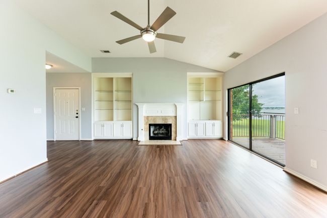 Unfurnished living room featuring ceiling fan, lofted ceiling, built in features, dark wood finished floors, and a premium fireplace | Image 10