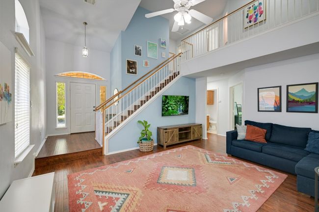 Living area featuring high vaulted ceiling, stairway, healthy amount of natural light, a ceiling fan, and wood finished floors | Image 4
