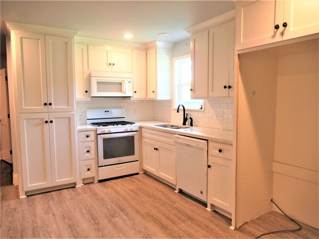 Kitchen with decorative backsplash, light countertops, white appliances, a sink, and light wood-style floors | Image 9